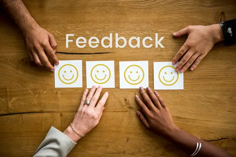 Imagem ilustrando a cultura do feedback, mostrando mãos com cartões sorridentes e a palavra 'Feedback' em destaque sobre uma mesa de madeira.